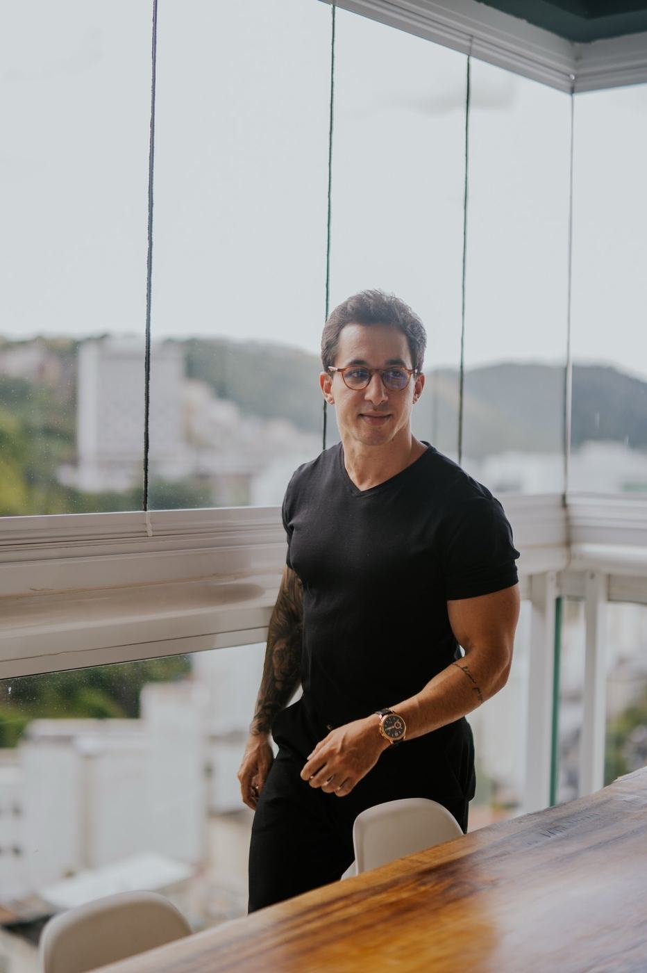 Fábio Coelho de pé junto à janela, com Juiz de Fora ao fundo